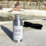 Swim Savvy bottle styled with towel and accessories, evoking a clean and fresh summer feel.
