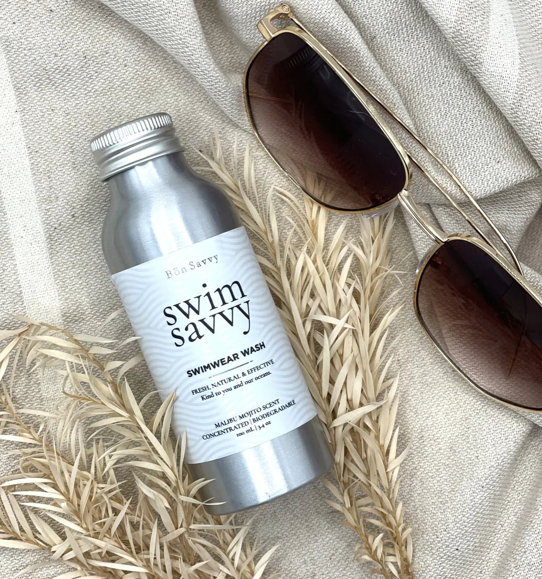 Swim Savvy Laundry Liquid and wash bag on a natural surface with summer essentials.