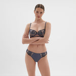 Model shown at an angle wearing Intrigue Bikini Brief Cinder Blue, emphasising couture style and scalloped edges at The Foundation.
