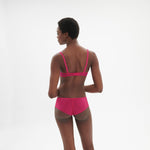 Model striking a playful pose in Intrigue Shorty Brief Disco Pink by Simone Perele, focusing on scalloped edges from The Foundation.
