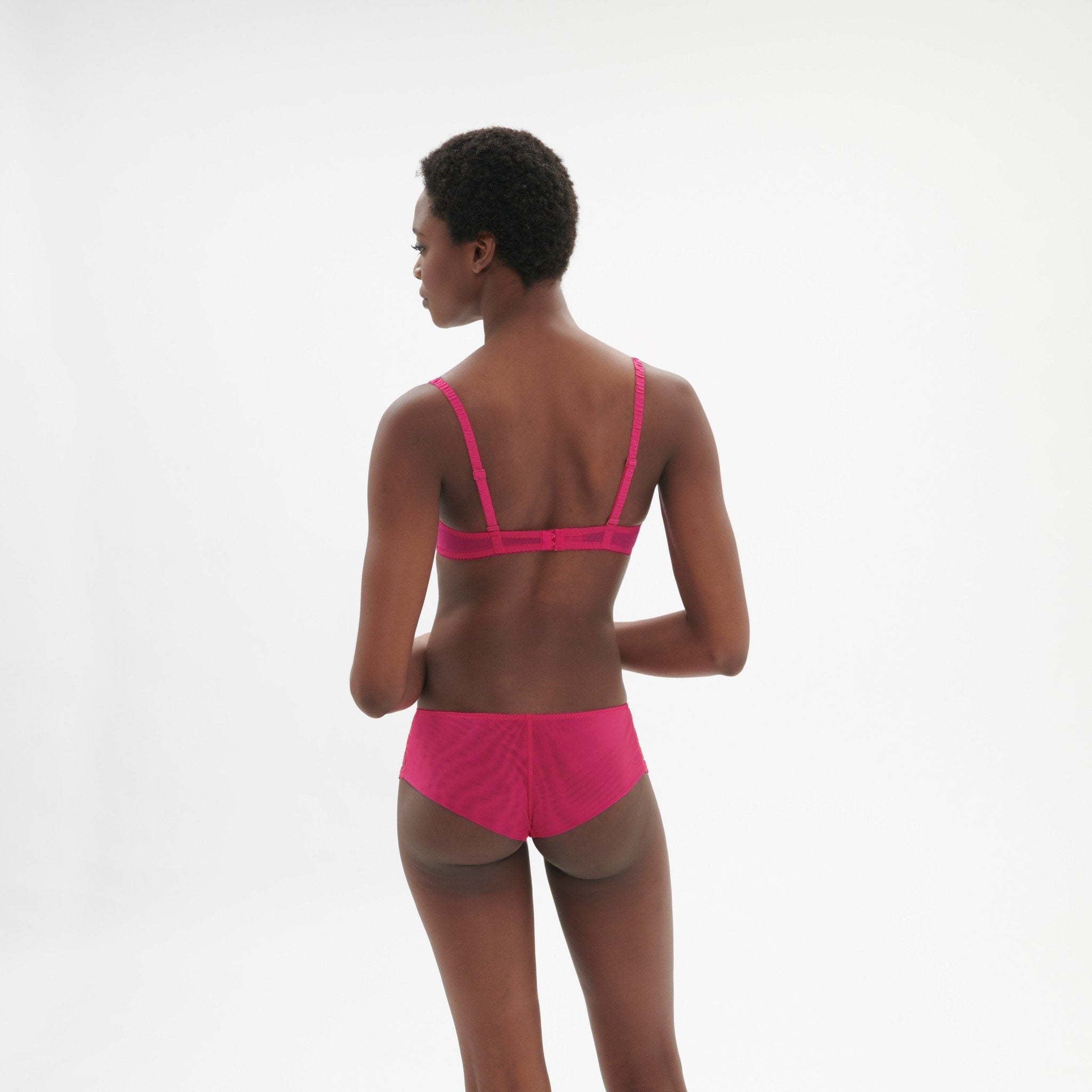 Model striking a playful pose in Intrigue Shorty Brief Disco Pink by Simone Perele, focusing on scalloped edges from The Foundation.
