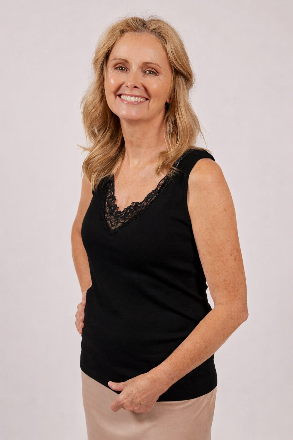 Woman wearing a black sleeveless top with lace details on a plain background