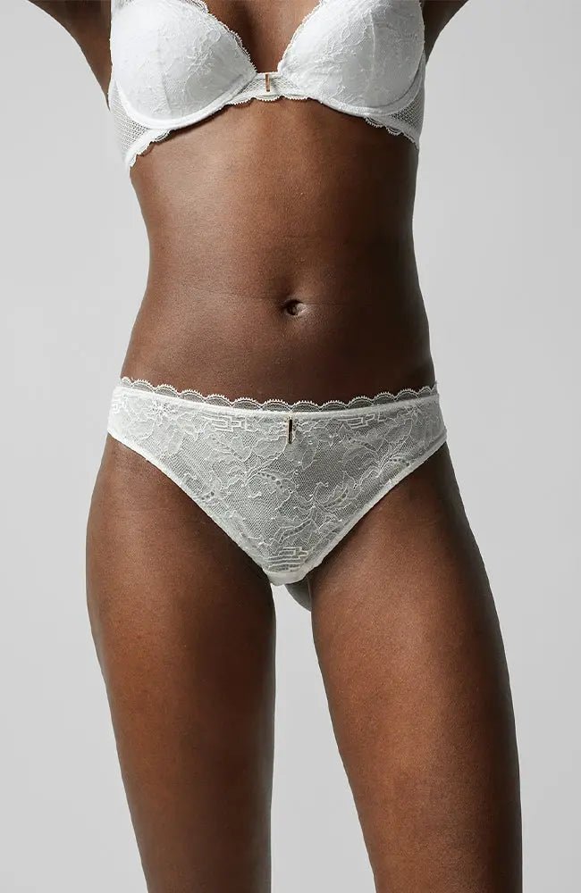 Front view of the Waltz Tanga Brief Milk Ivory from The Foundation – mid-rise lace thong with delicate scalloped trim and sheer floral panelling.