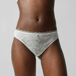 Front view of the Waltz Tanga Brief Milk Ivory from The Foundation – mid-rise lace thong with delicate scalloped trim and sheer floral panelling.