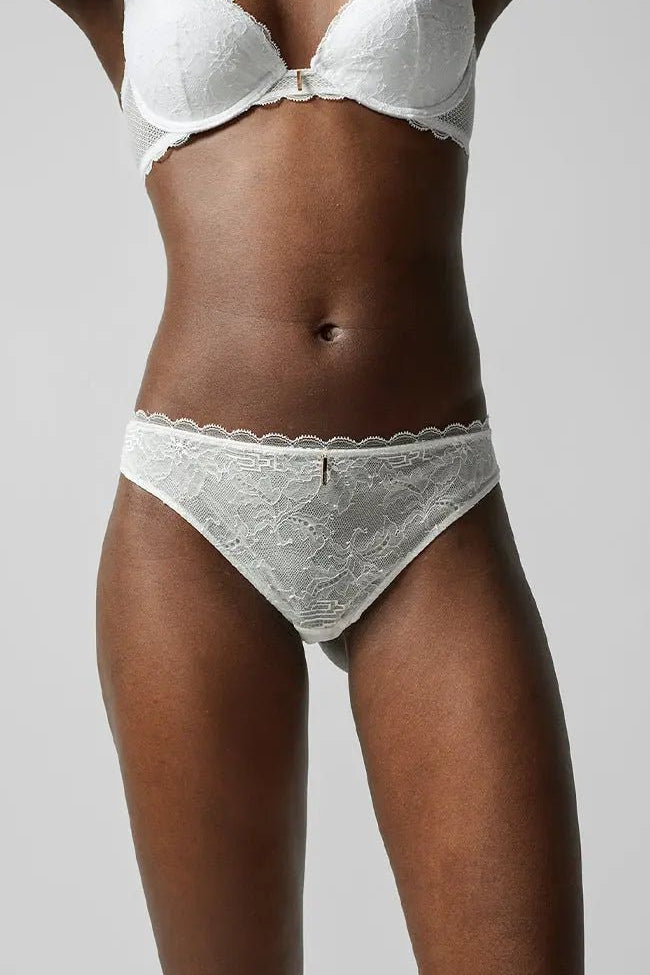 Front view of the Waltz Tanga Brief Milk Ivory from The Foundation – mid-rise lace thong with delicate scalloped trim and sheer floral panelling.