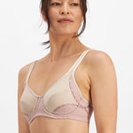 Studio image of woman smiling in the Electrify Mesh Underwire Sports Bra Soft Powder, available at The Foundation.