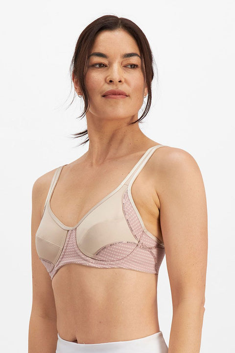 Studio image of woman smiling in the Electrify Mesh Underwire Sports Bra Soft Powder, available at The Foundation.