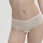 Model wearing Simone Pérèle Karma Shorty Brief in Natural from The Foundation, mid-rise lace design with cheeky back and scalloped edge detail. front view