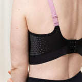Side-back angle of model wearing Triaction Control Lite Black sports bra, featuring adjustable multi-wear straps
