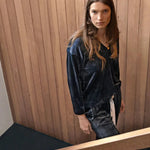 Woman in a dark blue velvet outfit standing against a wooden paneled wall.