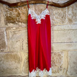 Kathryn Silk Chemise in rouge red with white lace trim, displayed hanging on a stone background.