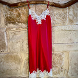 Kathryn Silk Chemise in rouge red with white lace trim, displayed hanging on a stone background.