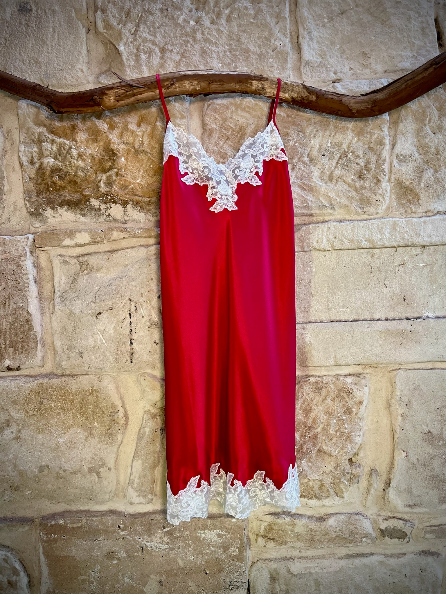 Kathryn Silk Chemise in rouge red with white lace trim, displayed hanging on a stone background.