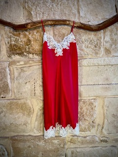 Kathryn Silk Chemise in rouge red with white lace trim, displayed hanging on a stone background.