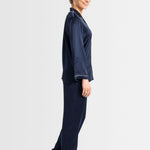 Side view of model in navy silk pyjamas showing long sleeves and pants with contrast trim.