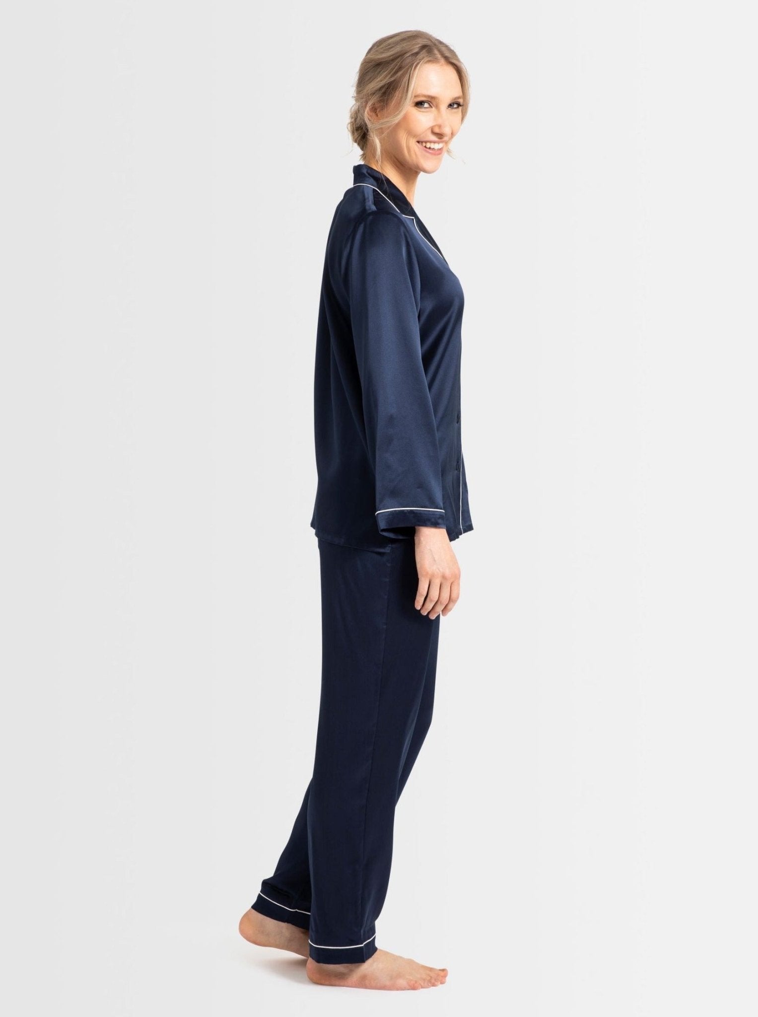 Side view of model in navy silk pyjamas showing long sleeves and pants with contrast trim.