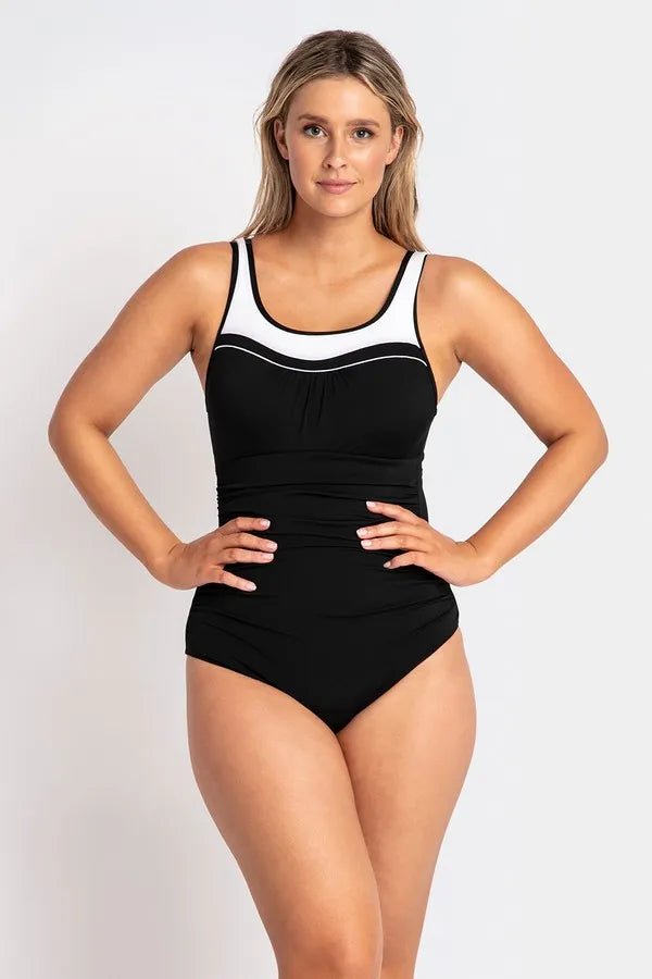 Woman modeling the black POOLPROOF mastectomy scoop one-piece swimsuit with white piping and side gathers.